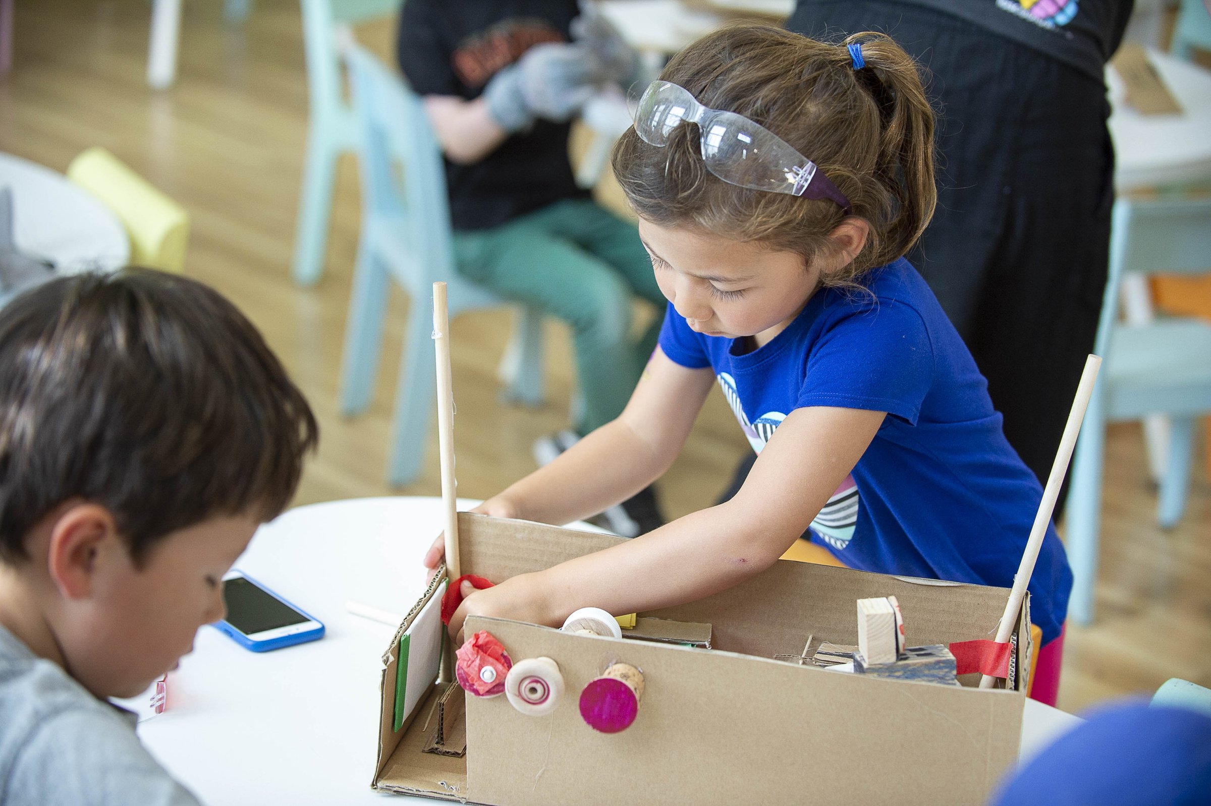 A student wearing safety goggles building a cardboard model at an extended-care table