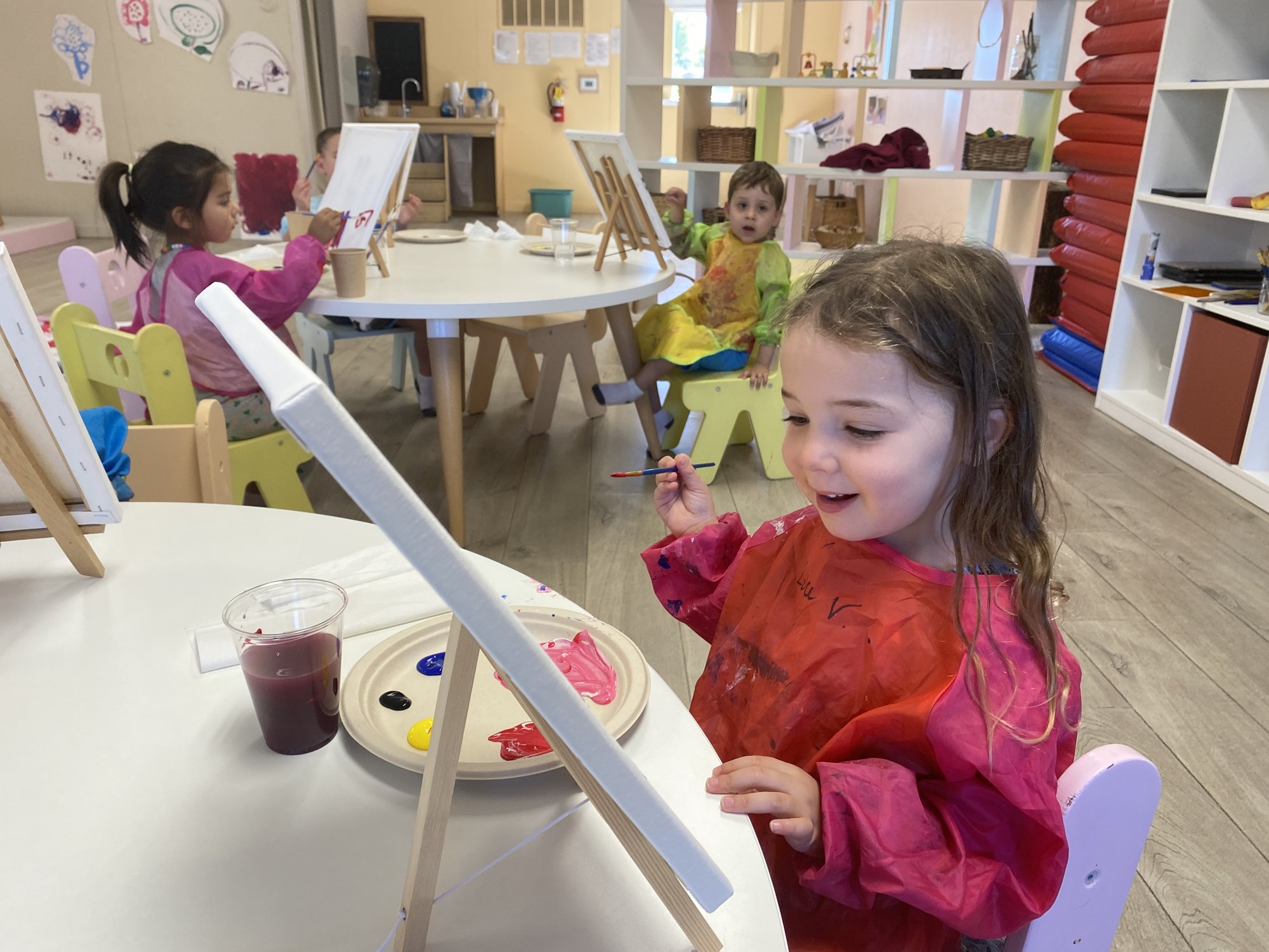 A young camper in a red smock painting at an easel