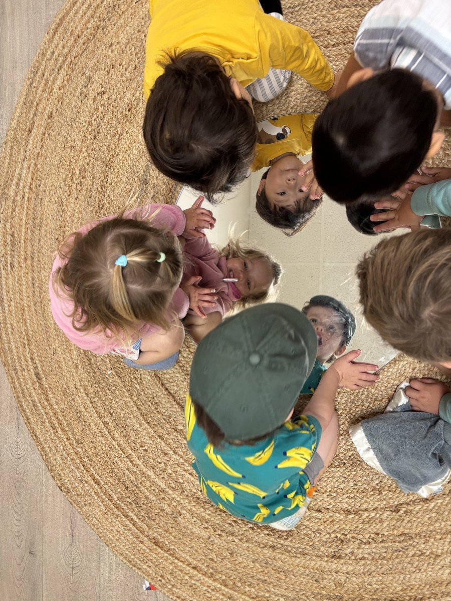 Students seen from above sitting in a tight circle on a round jute rug