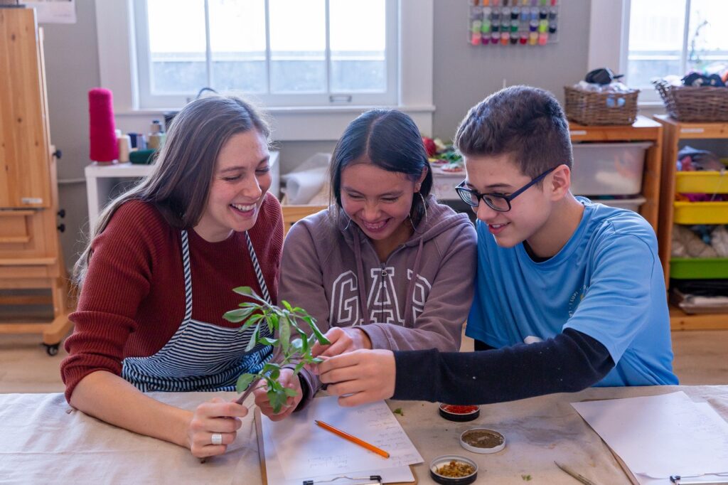 Three La Scuola teachers laughing together over a plant cutting